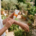 Kobieta delikatnie nakłada krem spf 50 La Roche-Posay na przedramię, przygotowując się na słońce.